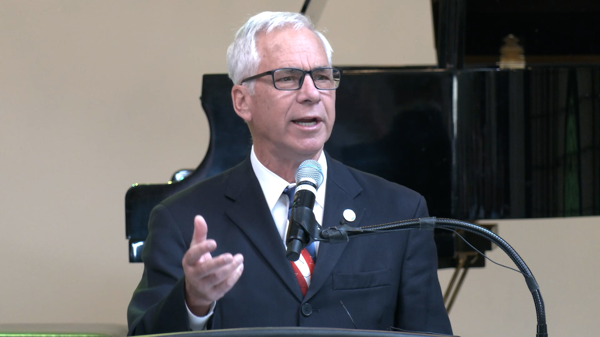 Mayor in blue suit and American flag tie speaking at a podium